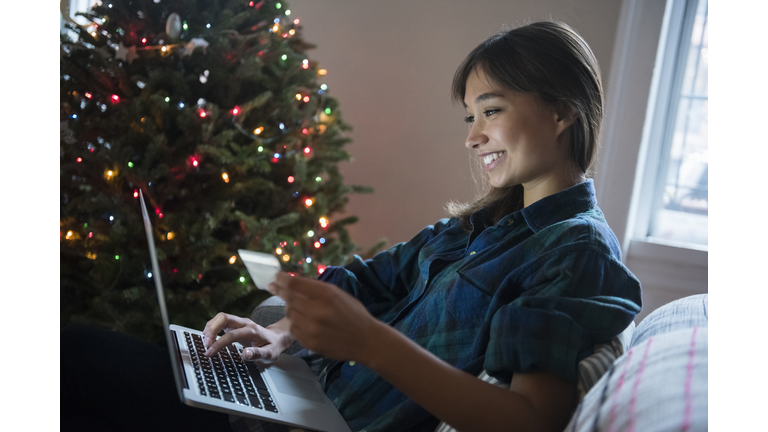 Mixed Race woman online shopping with laptop near Christmas tree