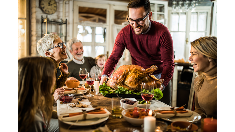Young happy man serving Thanksgiving turkey for his family at dining table.