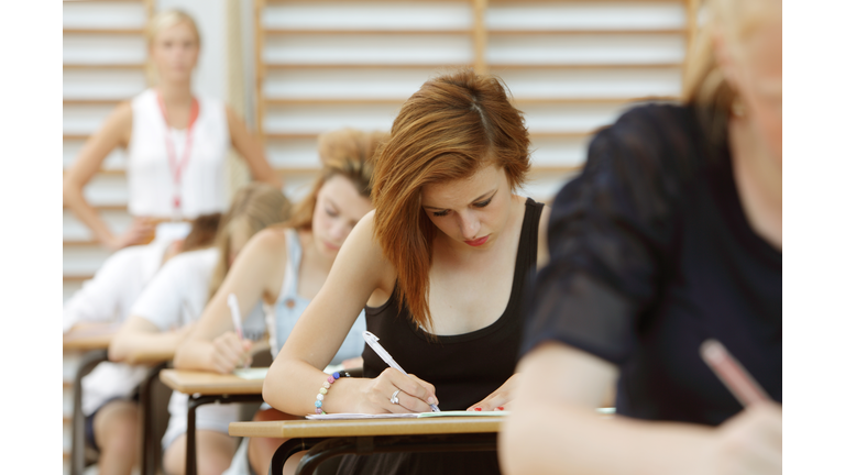 Students taking exam, teacher in background