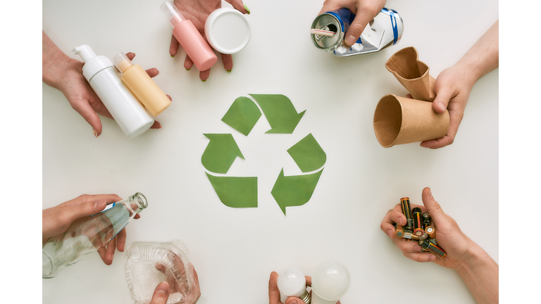 Your life improved. Top view of many hands holding different waste, garbage types with recycling sign made of paper in the center over white background