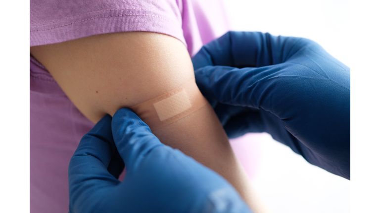 A gloved doctor or health care professional applies a patch or adhesive bandage to a girl or young woman after vaccination or drug injection. The concept of medicine and health care, vaccination and treatment of diseases. First aid services.