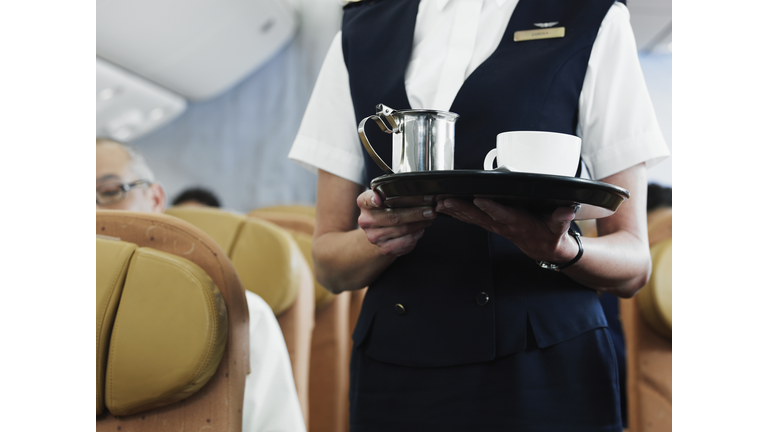 Flight attendant holding tray with coffee, mid section