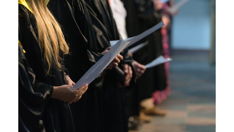 Choir singers holding musical score and singing on student graduation day in university, college diploma commencement