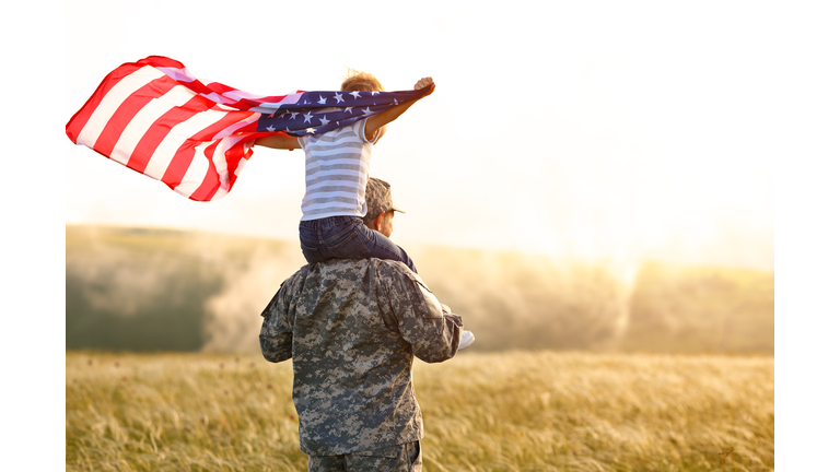 Excited child sitting with american flag on shoulders of father reunited with family