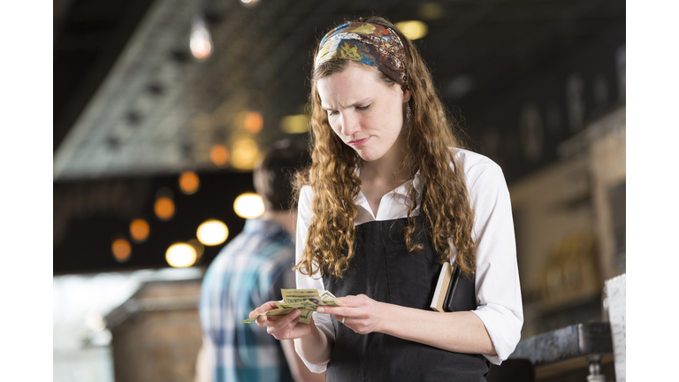 Frustrated young waitress counting cash tips after shift