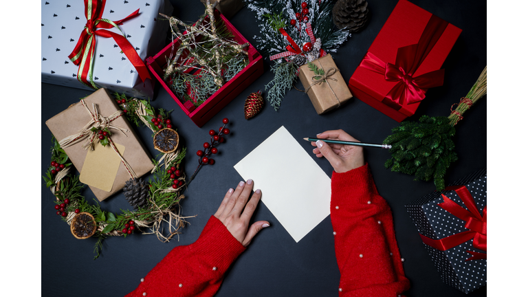 Christmas decorations and presents on black background with a hand writing a Christmas card