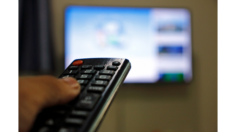 Hand holding remote control of television. Man watching TV at home and using remote control.