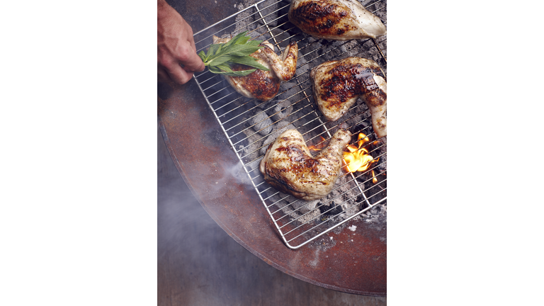 Mans hand grilling Guam chicken legs on barbecue