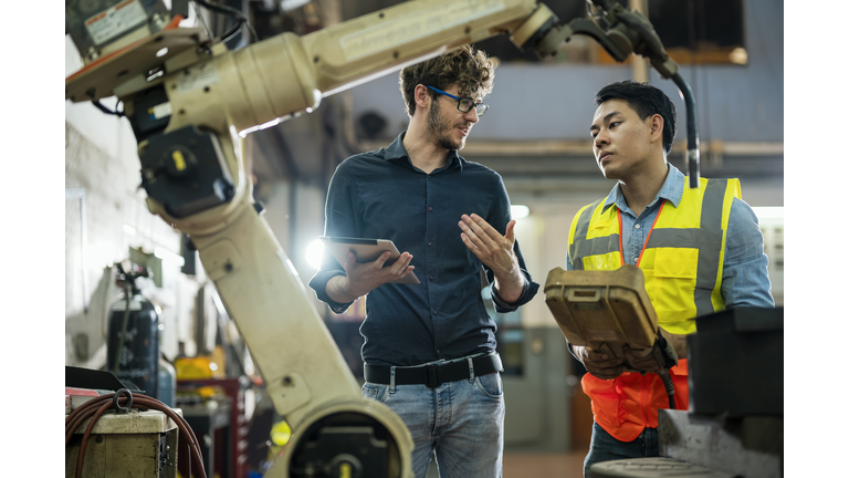 Software engineer explaining to controlling robotic welding process to welder in factory.