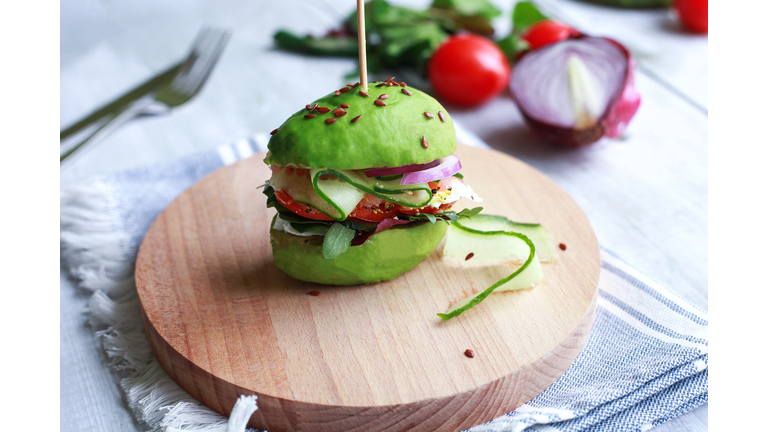 Healthy vegan meal: avocado burger with cucumber, tomato, onion, greens and seeds on wooden plate. Concept of veganism.