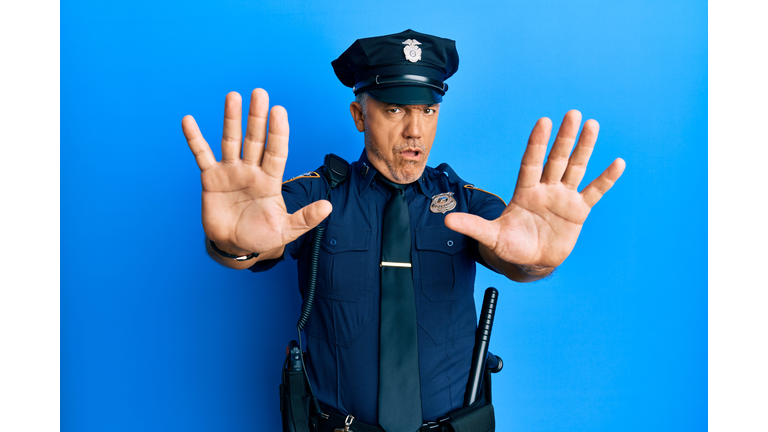Handsome middle age mature man wearing police uniform doing stop gesture with hands palms, angry and frustration expression