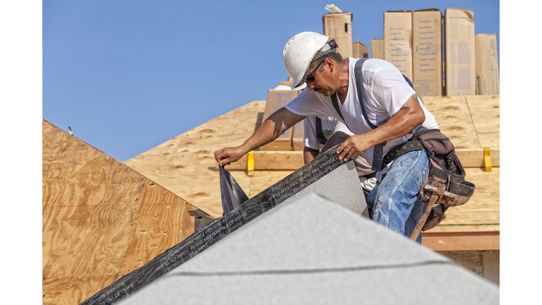 Roofer tears off protective cover of underlayment on a new roof