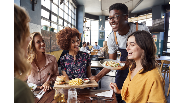 Waiter Serving Group Of Female Friends Meeting For Drinks And Food In Restaurant