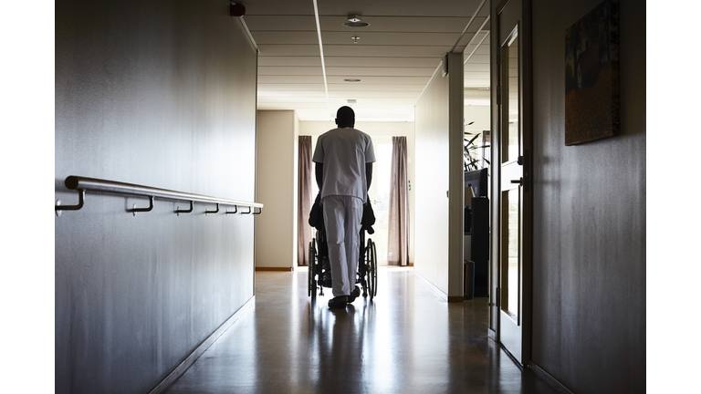 Full length rear view of male nurse pushing senior man on wheelchair at hospital corridor