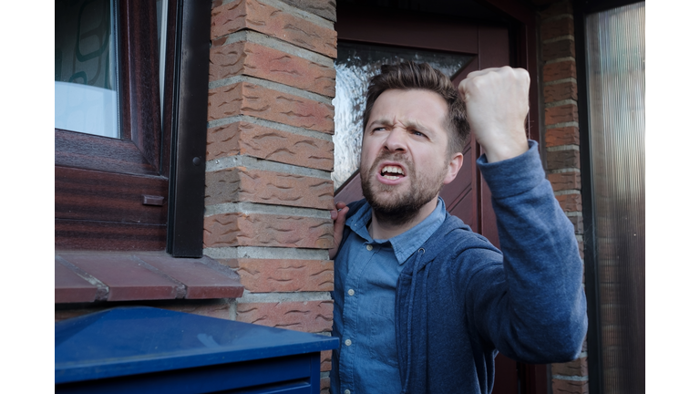 Angry upset young male neighbor with fist in air, open mouth yelling.