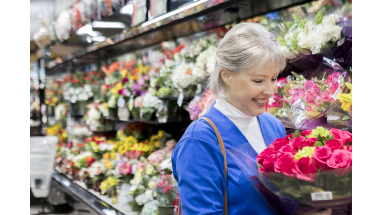 Senior woman inspects bouquet of roses in grocery store