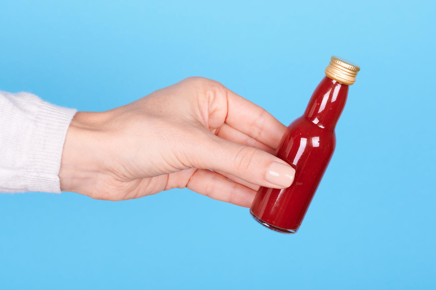 Hand with red hot sauce in bottle on blue background.
