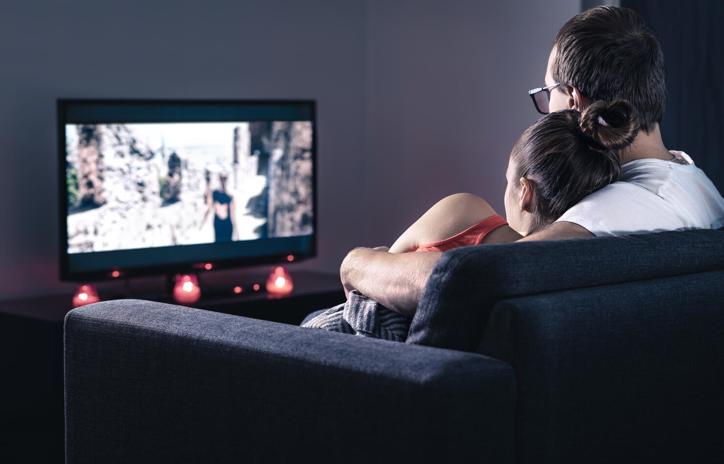 Couple watching movie or series. Online streaming and VOD service in tv screen. Film stream or television show. Cuddling during comfy and romantic candle light date at home.