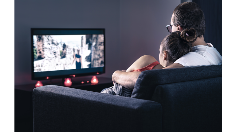 Couple watching movie or series. Online streaming and VOD service in tv screen. Film stream or television show. Cuddling during comfy and romantic candle light date at home.