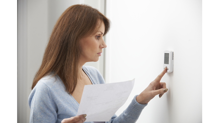 Worried Woman Turning Down Central Heating Thermostat