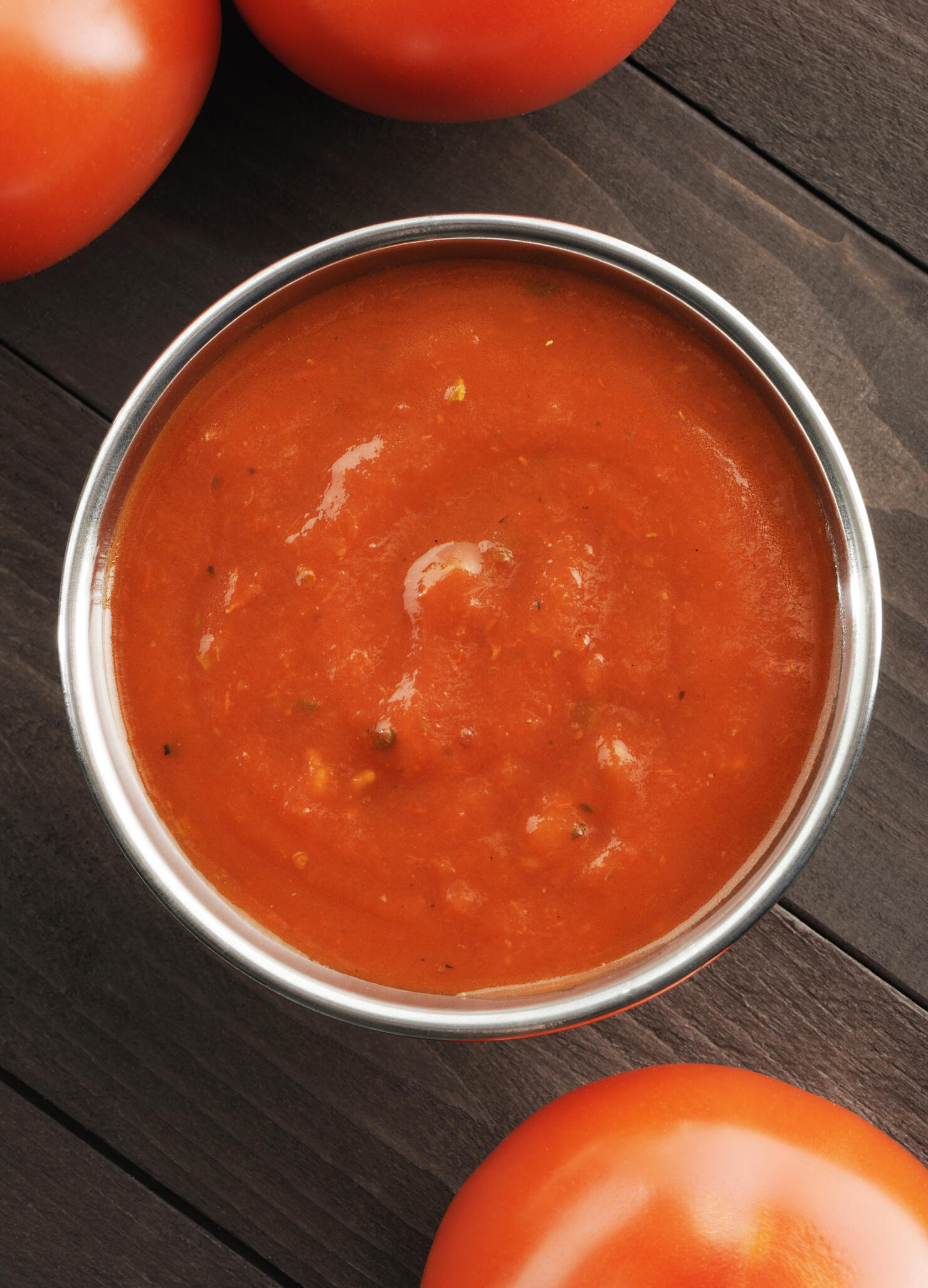 Overhead view of a bowl of tomato sauce next to tomatoes