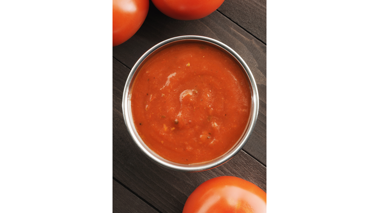 Overhead view of a bowl of tomato sauce next to tomatoes