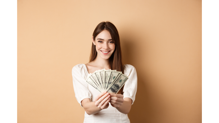 Portrait of young woman holding paper currency against beige background
