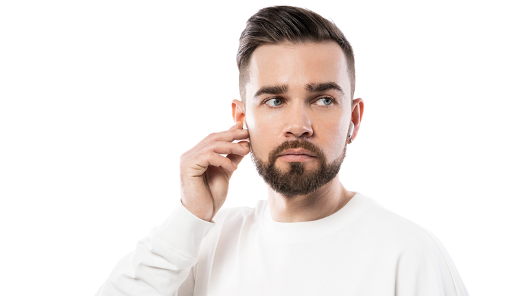 Handsome bearded man in white clothes  using wireless earbuds on white background