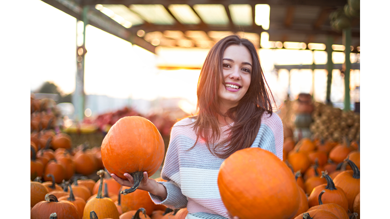 Fashionable beautiful young girl at the autumn pumpkin patch background. Having fun and posing