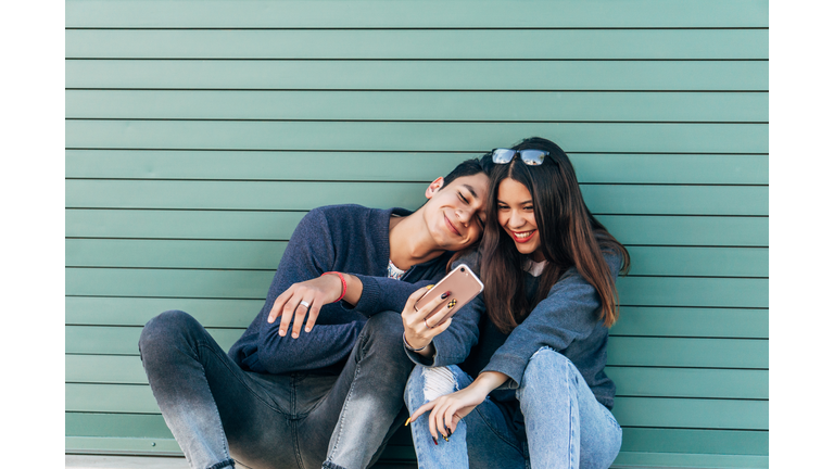 YOUNG COUPLE SITTING TAKING A SELFIE, GREEN BACKGROUND, YOUNG LOVE, RELATIONSHIP, VALENTINE'S DAY