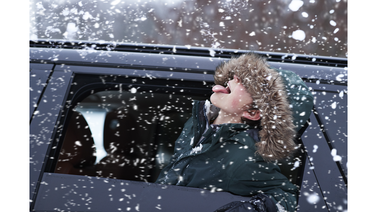 Boy tasting snow through car window during snowfall