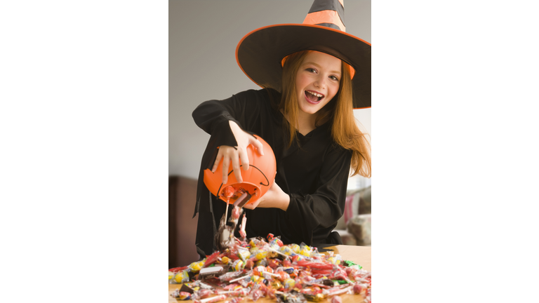 Caucasian girl in witch costume dumping out Halloween candy