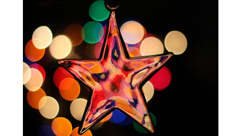 Close-up of a star-shaped Christmas ornament hanging against defocused multicolored lights on black background