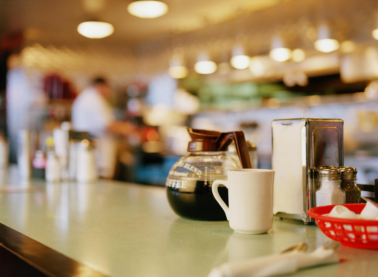 Diner counter top with coffee pot and cup next to napkin dispenser