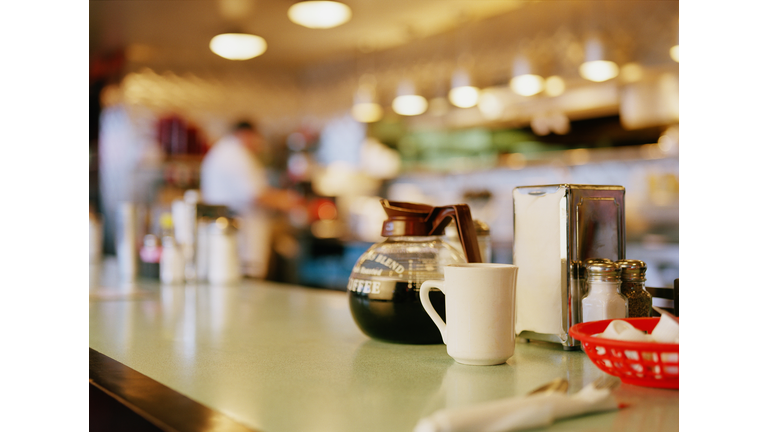 Diner counter top with coffee pot and cup next to napkin dispenser