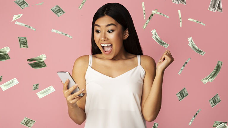 Big Win. Asian Girl Celebrating Victory With Smartphone Under Dollar Money Shower