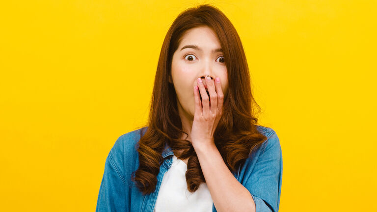 Portrait Of Surprised Young Woman With Hands Covering Mouth Against Yellow Background