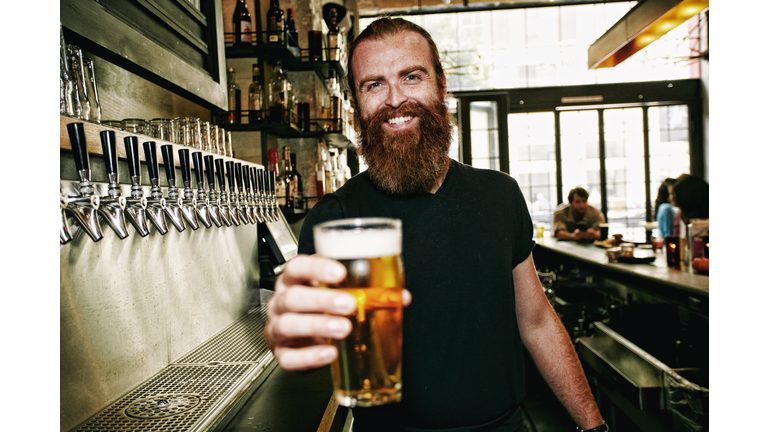 Smiling Caucasian bartender serving beer at bar