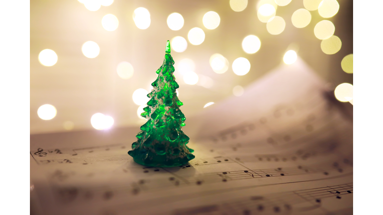 Old sheet with Christmas music notes as background against blurred lights. Christmas music concept