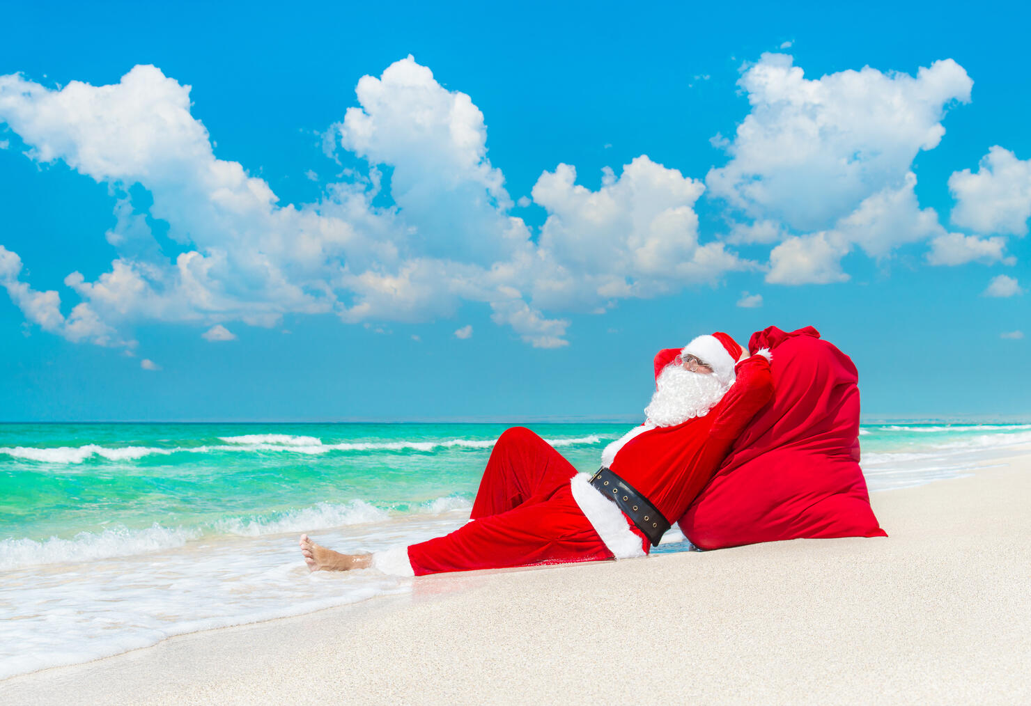 Santa Claus sunbathing at sack full of gifts at beach