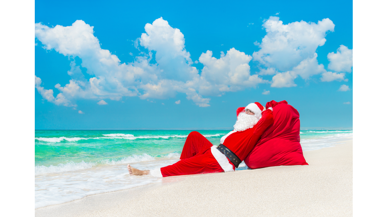 Santa Claus sunbathing at sack full of gifts at beach