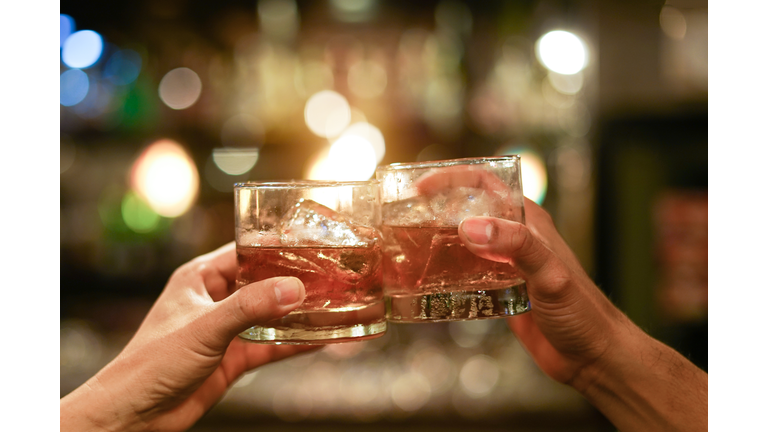 two men clinking glasses of whiskey drink alcohol beverage together at counter in the pub