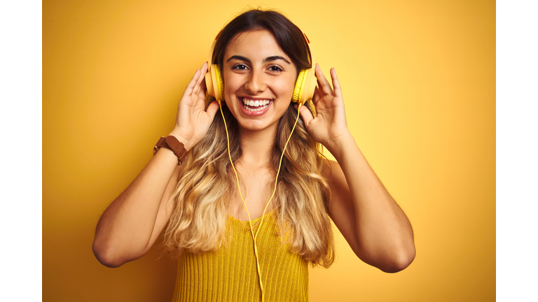 Young beautiful woman wearing headphones over yellow isolated background with a happy face standing and smiling with a confident smile showing teeth