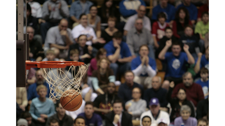 Basketball ball and backboard with fans in the background.