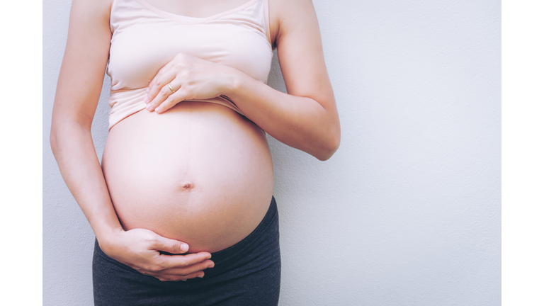 Midsection Of Pregnant Woman Touching Stomach Against White Background