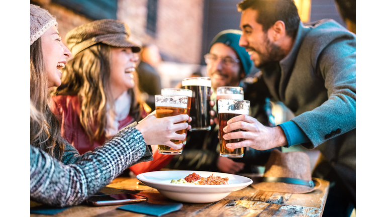Friendly guys approaching happy girls at brewery pub outdoor on winter time - Friendship concept with young people having drunk fun together drinking beer at happy hour promotion - Vivid color filter