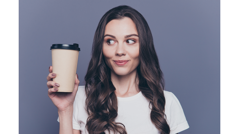 Close-up portrait of attractive pretty lovely stylish nice cute cheerful curly-haired brunette girl in casual white t-shirt, holding, looking at paper-cup coffee, isolated on grey background