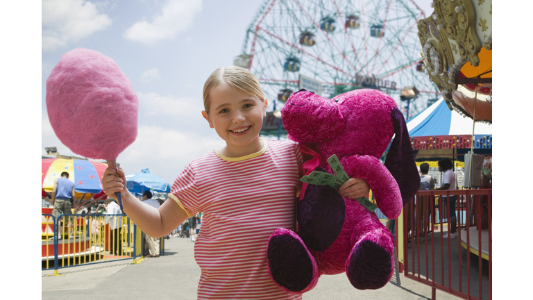 Young girl holding cotton candy and fair prizes