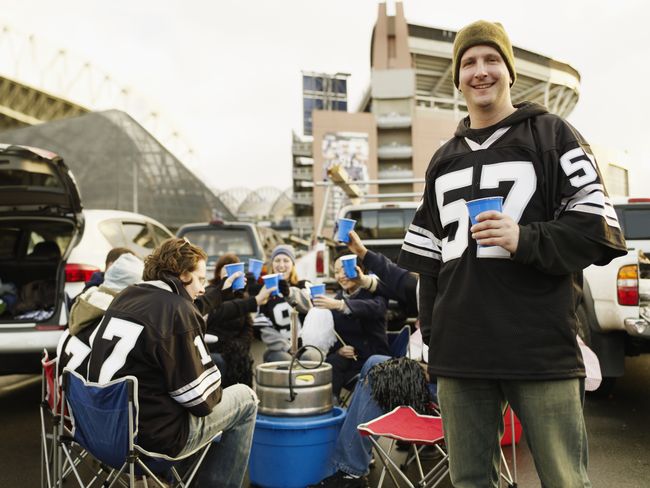 Man holding drinks at tailgate party, friends in background