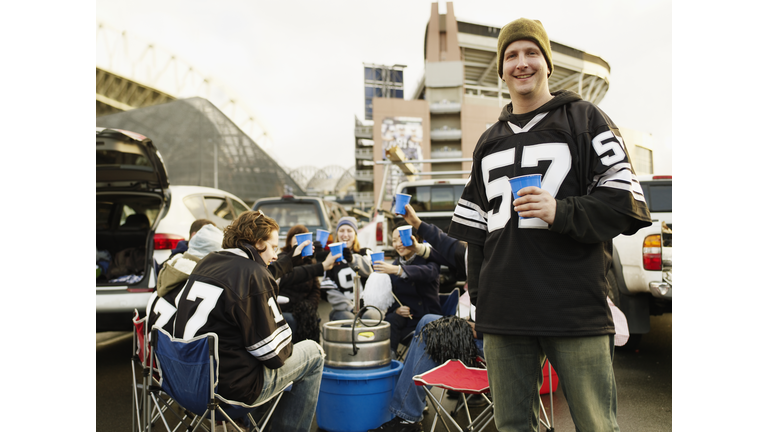 Man holding drinks at tailgate party, friends in background
